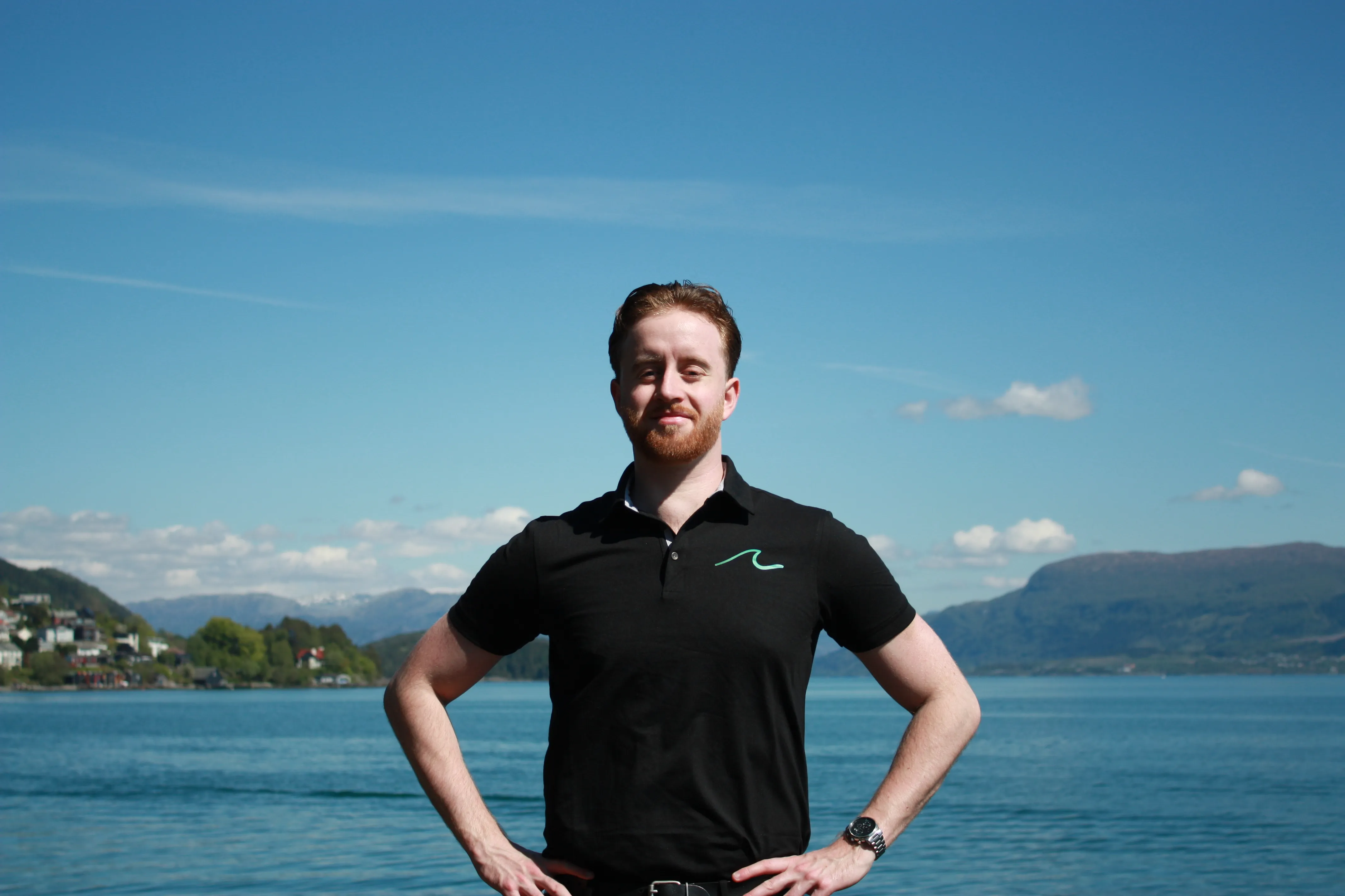 Grunderen bak Havøyet i sort firmaskjorte, med fjorden og fjellene bak seg.